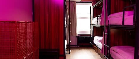 A dormitory room with bunk beds, a radiator, and a curtain.
