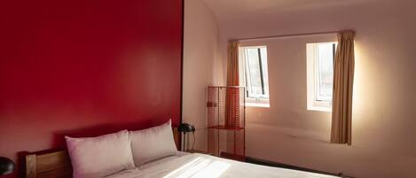 A room with a wooden bed, a red wall, and a single window with curtains.