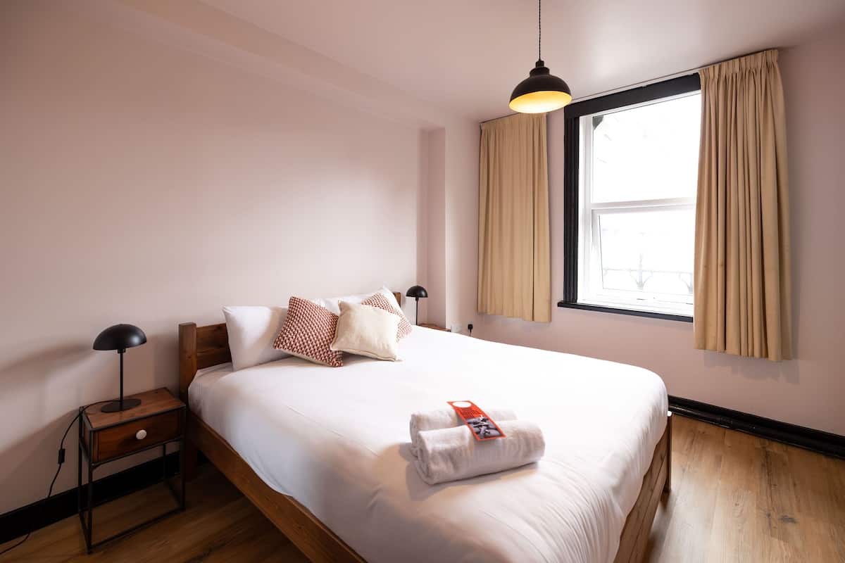 A neatly made bed with white linens, a wooden headboard, and a bedside table with a lamp.