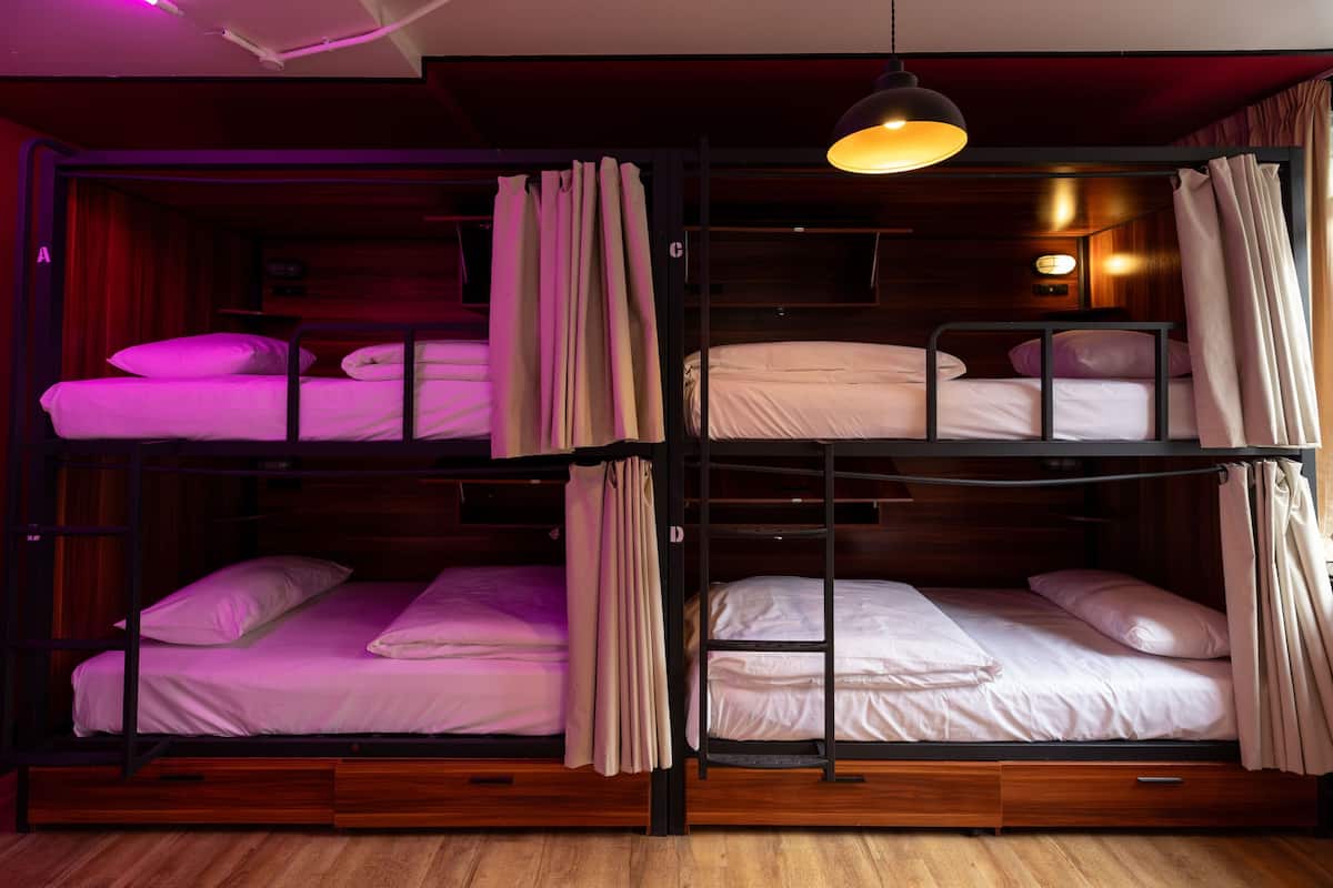 A bunk bed room with wooden flooring, a hanging light fixture, and curtains on the windows.