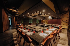A modern restaurant with a long communal table, individual seating, and a central island.