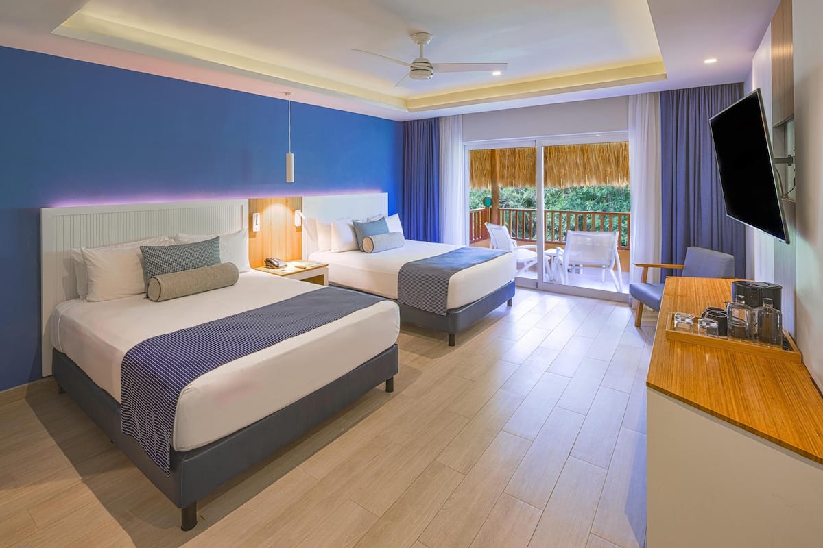 A hotel room with two beds, a desk, a TV, and a balcony with a view.