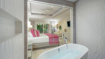 Un baño moderno con una bañera independiente, cabina de ducha con paredes de vidrio y una habitación con cama y manta roja a la vista.