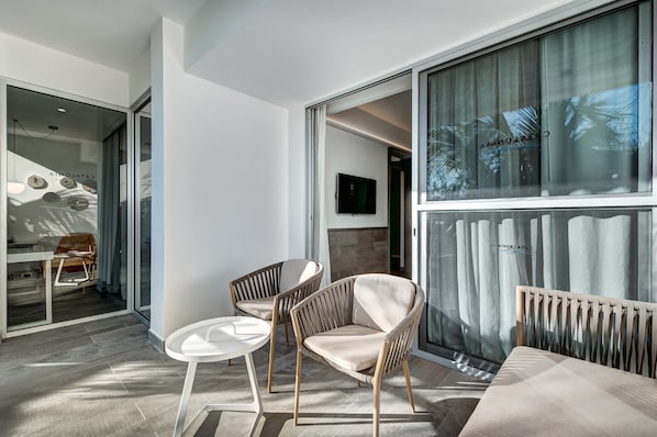 A modern interior with two wicker chairs and a small white table, large windows with curtains, and a visible television.
