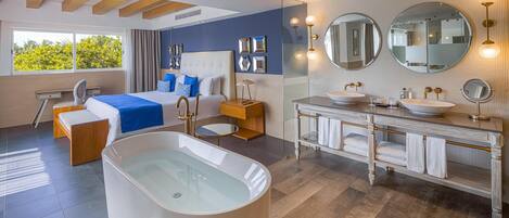 Une chambre d’hôtel moderne dotée d’une grande baignoire, d’un lit double, d’un bureau et d’une salle de bain avec un meuble-lavabo et deux vasques.