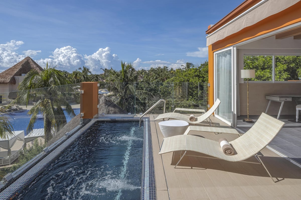 A rooftop infinity pool with lounge chairs, a glass-enclosed dining area, and a view of a tropical landscape.