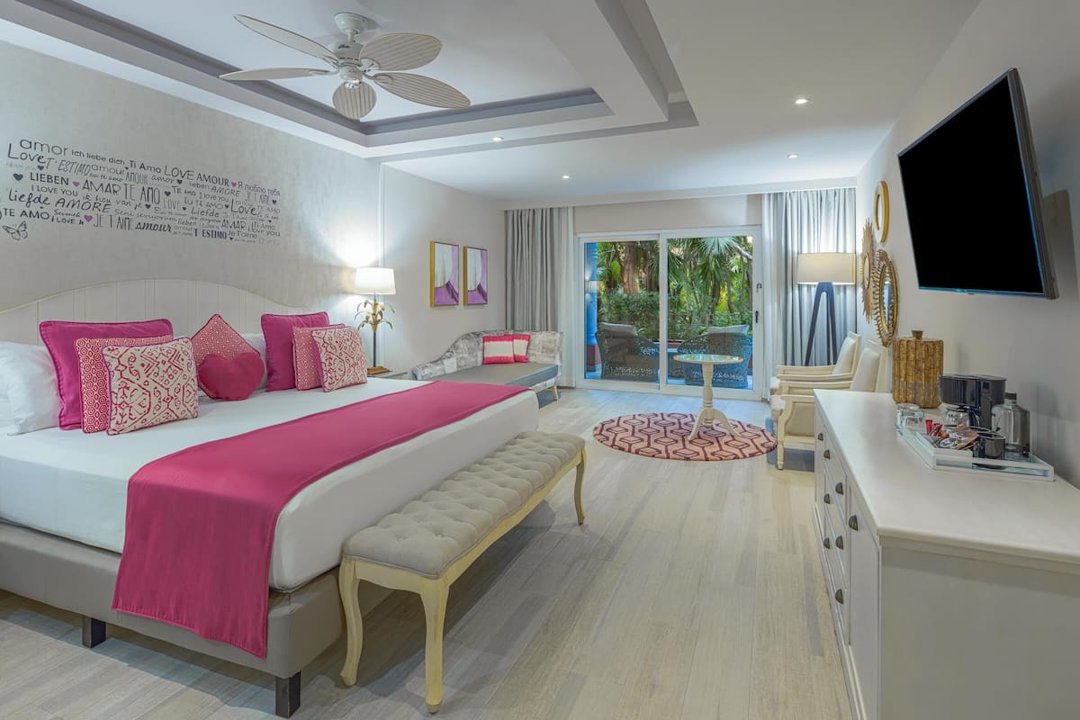 A modern hotel room with a large bed, a bench, a desk, a TV, and a balcony with a view.