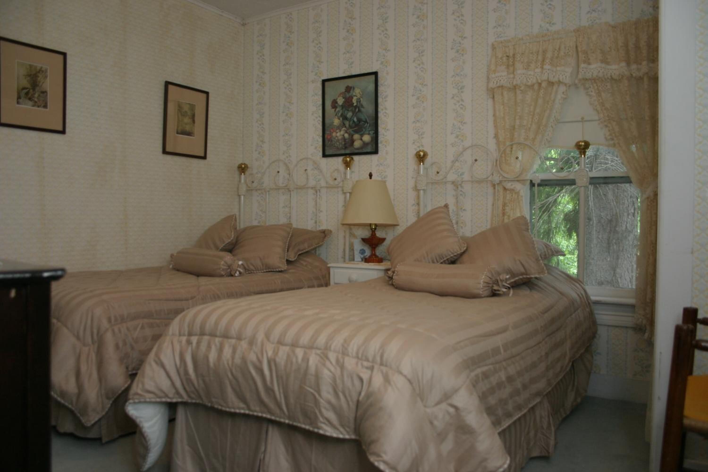 Une chambre avec deux lits, une table de chevet avec une lampe et une fenêtre avec des rideaux.