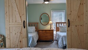 A bedroom with two beds, a dresser, a ceiling fan, and a window with blinds. - The Inn at Starlight Lake (Starlight)