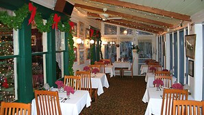 A restaurant with multiple tables and chairs, decorated with Christmas garlands and lights. - The Inn at Starlight Lake (Starlight)