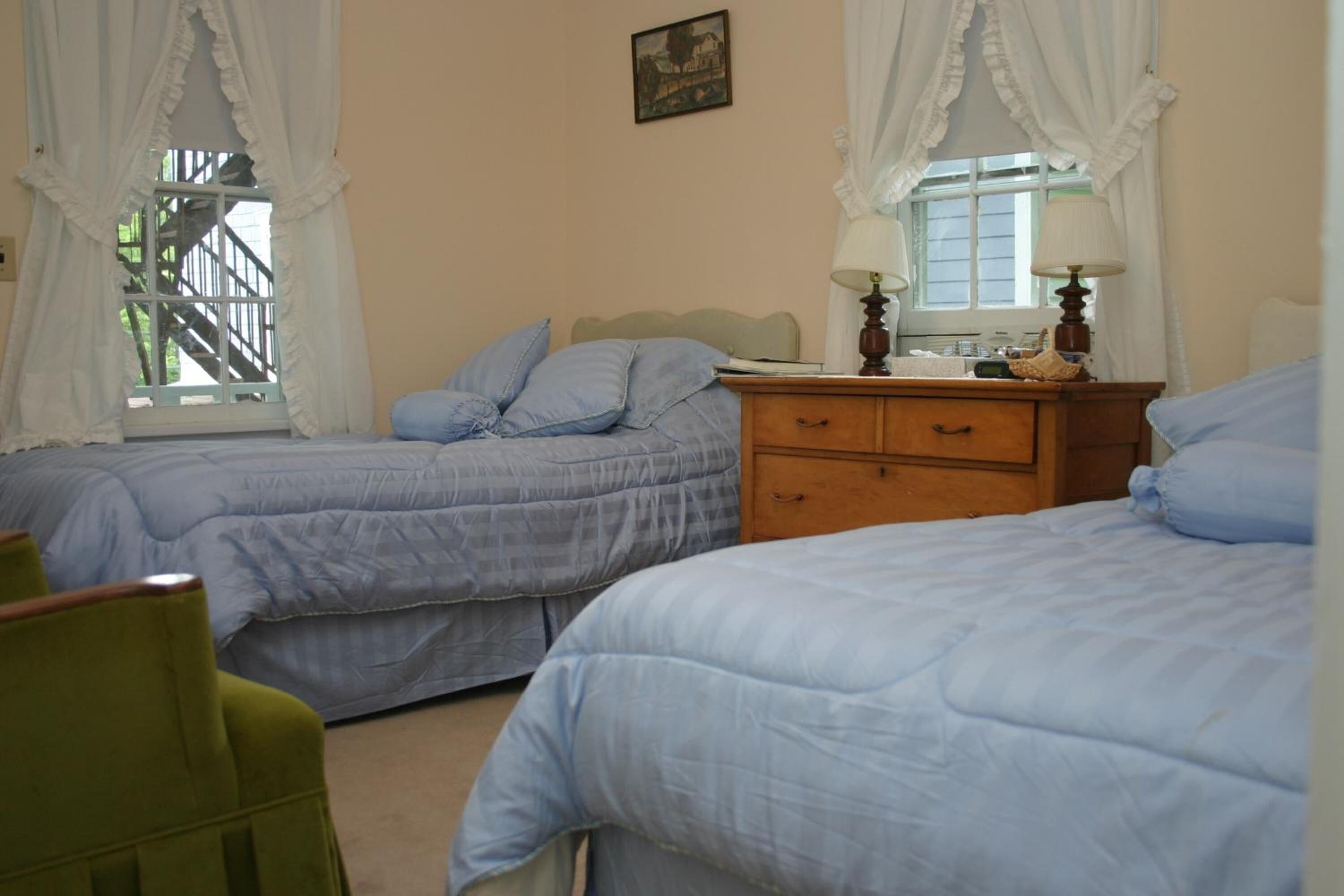 A bedroom with two beds, a wooden dresser, and a chair.