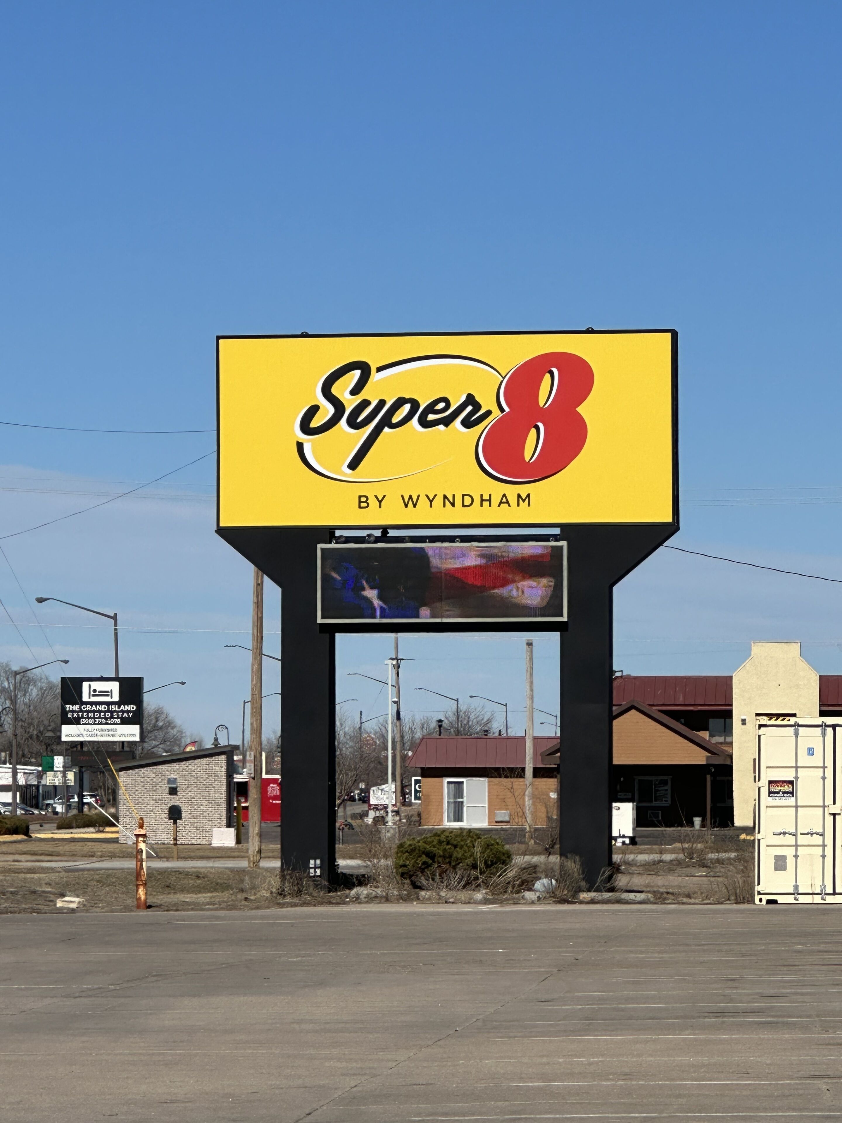Een reclamebord voor 'Super 8 by Wyndham' met een helder uitzicht op de omgeving, inclusief een gebouw en een parkeerplaats.