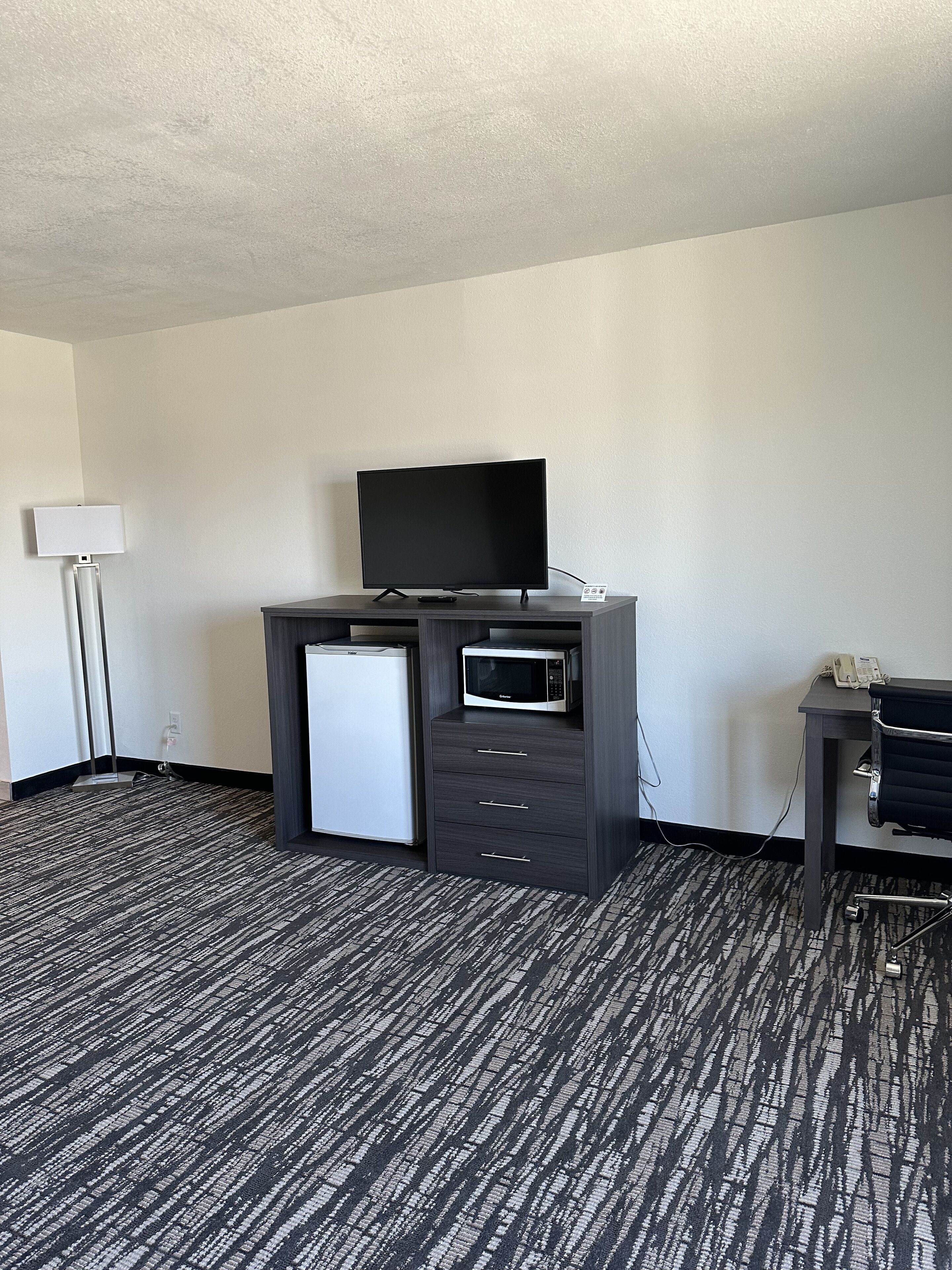Quarto de hotel com televisão de tela plana, mini-geladeira, micro-ondas e escrivaninha com cadeira.