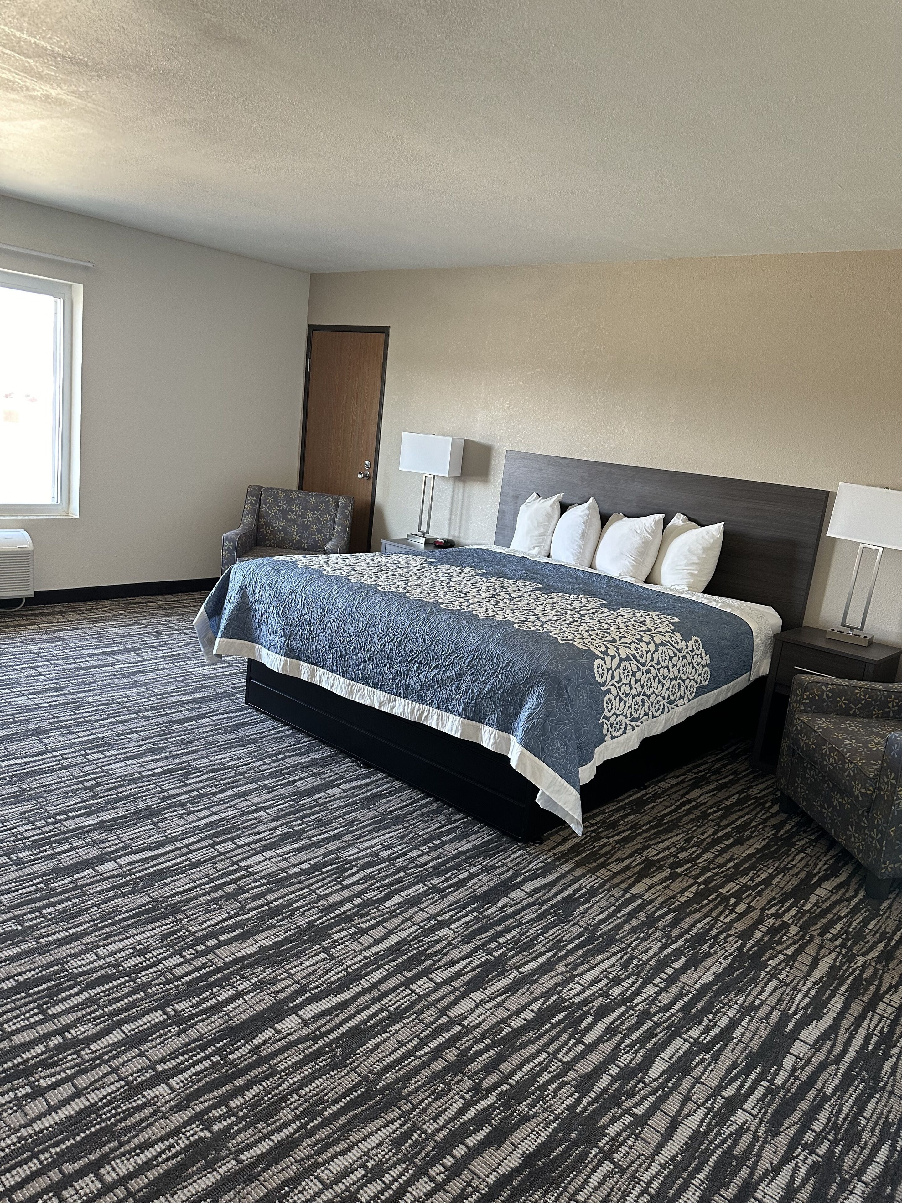 Une chambre d’hôtel avec un grand lit, une chaise, un bureau, une lampe et une porte.
