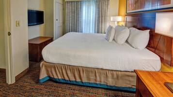 Quarto de hotel com cama grande, televisão fixada na parede, janela com cortinas e mesa de cabeceira.