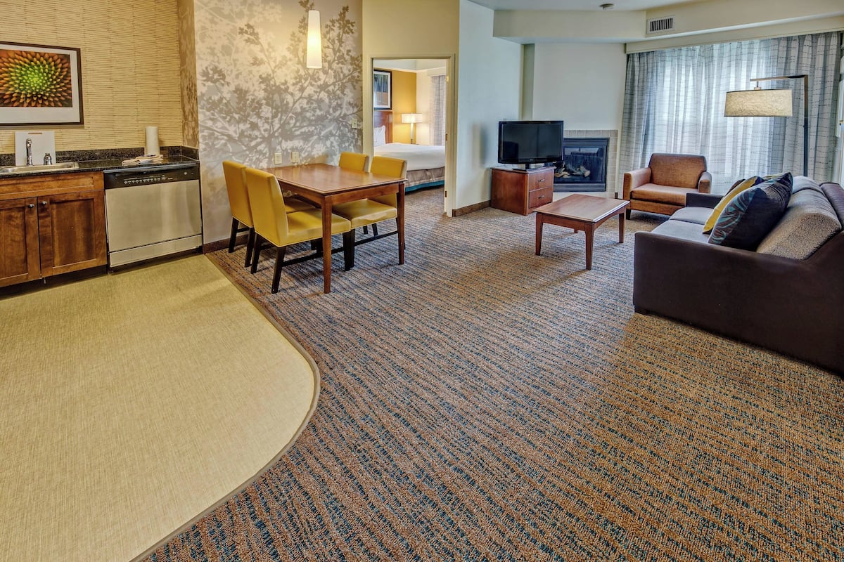 A hotel room with a dining area, a sofa, a television, and a fireplace.
