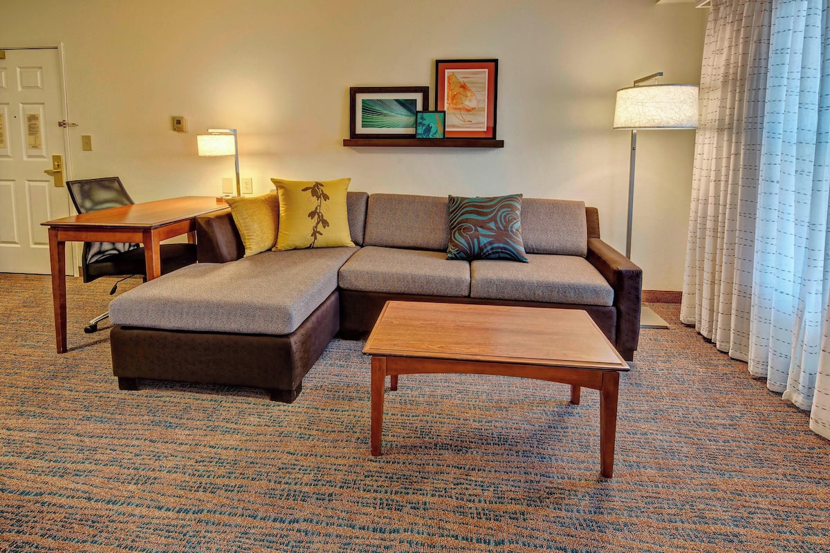 A living room with a sectional sofa, a small table, and a lamp.