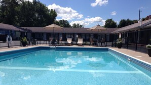 A rectangular swimming pool with a clear blue water surface, surrounded by lounge chairs and umbrellas, and a fence enclosing the area. - Moonlite Motel Niagara Falls (Niagara Falls)