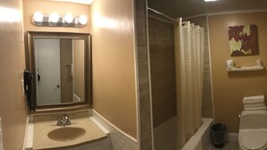 A bathroom with a vanity, sink, mirror with lights, shower curtain, toilet, and a towel rack. - Moonlite Motel Niagara Falls (Niagara Falls)