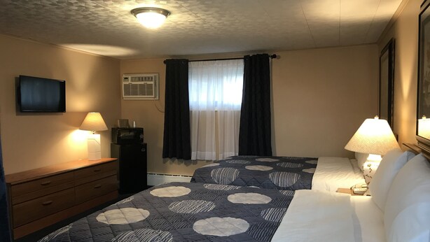 A hotel room with two beds, a flat-screen TV, a desk with a lamp, and a ceiling light. - Moonlite Motel Niagara Falls (Niagara Falls)