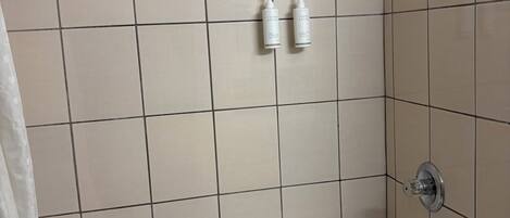 Une salle de bain avec une baignoire, une douche et deux bouteilles de shampoing.