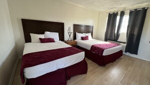A hotel room with two beds, each with a wooden headboard, white bedding, and maroon bed skirts. There is a nightstand with a lamp between the beds. - Hometown Inns North Hills (North Hills)