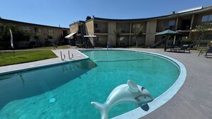 A swimming pool with a dolphin float, surrounded by a fenced area with lounge chairs and a building with balconies. - Hometown Inns North Hills (North Hills)