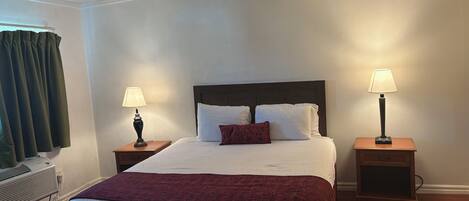 A neatly made bed with white and red bedding, two bedside lamps, and a wooden nightstand.