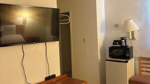 A compact room with a flat-screen TV mounted on the wall, a small refrigerator, a microwave, a wooden desk with drawers, and a chair. - Hometown Inns North Hills (North Hills)