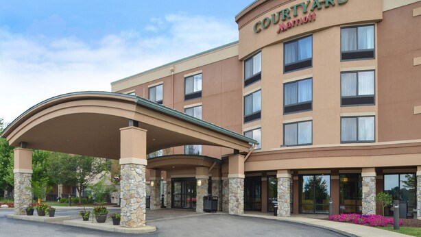 Courtyard Marriott -hotelli, jossa on katettu sisäänkäynti, kivipylväät ja maisemoitu alue, jossa on ruukuissa olevia kasveja.