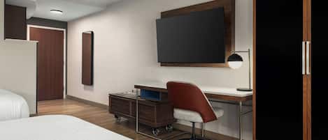 Habitación de hotel con una cama, un escritorio con silla, un armario y un televisor en la pared.