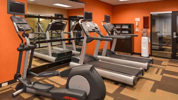 Une salle de sport équipée de tapis de course, de vélos elliptiques et d’un distributeur d’eau.