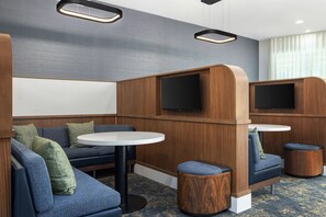 A modern hotel room with a sectional sofa, a round table, and two TV screens. - Courtyard by Marriott Pittsburgh Monroeville (Monroeville)