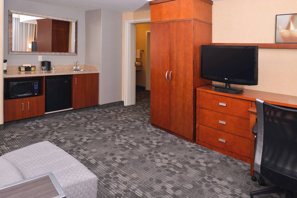 A hotel room with a kitchenette, a TV, a desk, and a chair.
