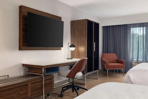 A hotel room with a large flat-screen TV mounted on the wall, a desk with a chair, a wardrobe, a single bed, and a window with curtains. - Courtyard by Marriott Pittsburgh Monroeville (Monroeville)