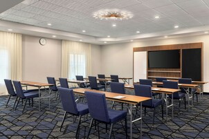 Un salón de conferencias con mesas, sillas, un reloj y una pantalla grande.