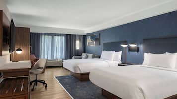 Habitación de hotel con dos camas, un escritorio, una silla, un televisor y un ventanal con cortinas.