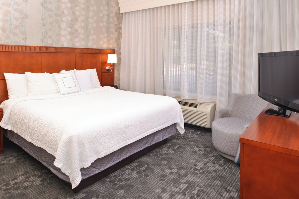 A hotel room with a large bed, a television, a chair, and a window with curtains.