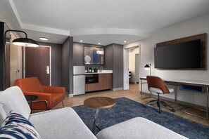 Quarto de hotel moderno com sofá, área de refeições, cozinha e televisão.