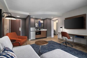 Una habitación de hotel moderna con sofá, comedor, cocina y televisor.