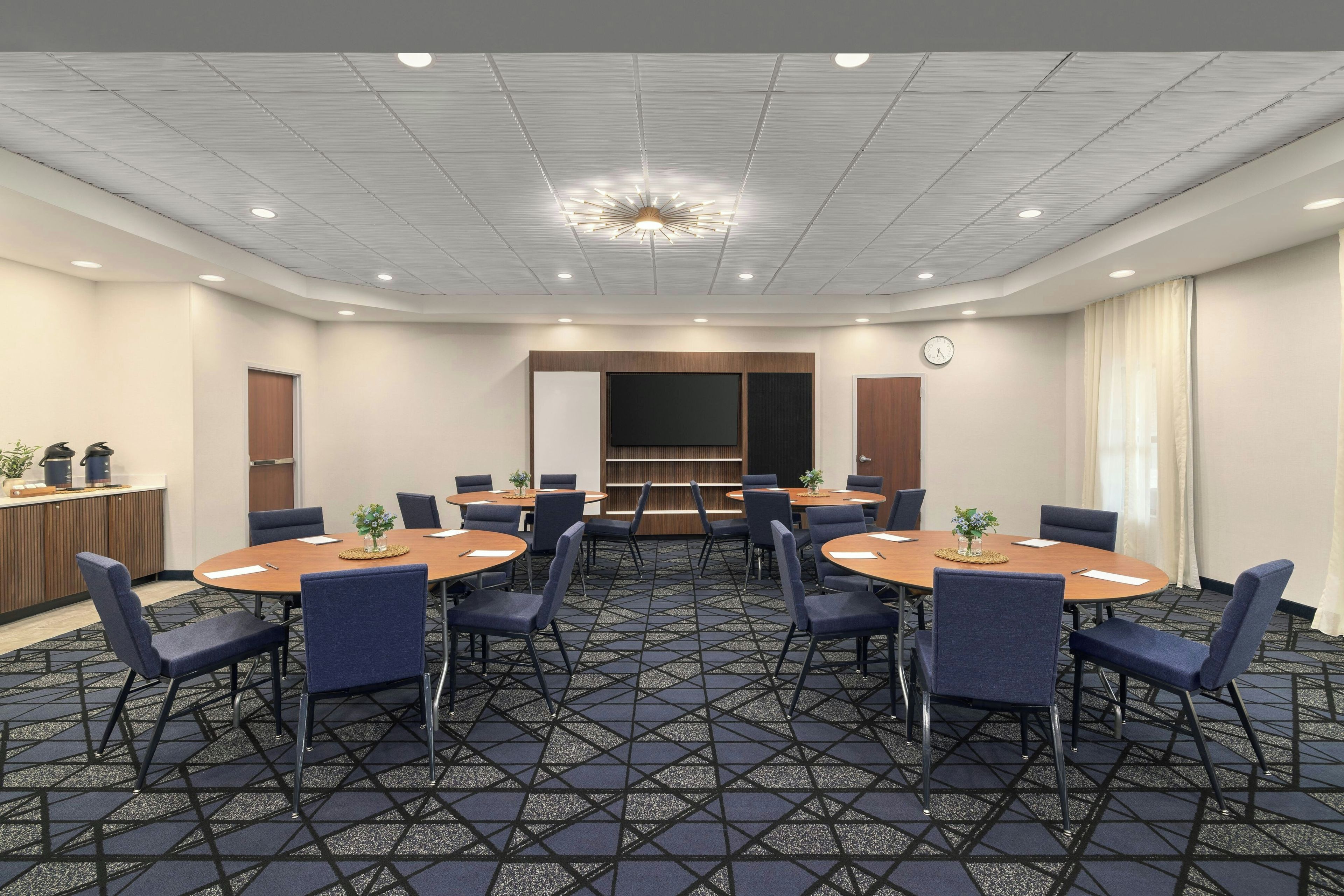 A conference room with round tables, chairs, a clock, and a ceiling light fixture.