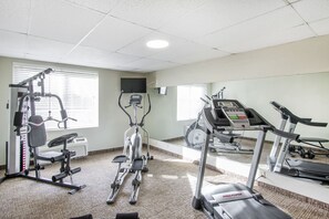 Een fitnessruimte met cardiotoestellen, gewichtapparatuur en een spiegelwand.