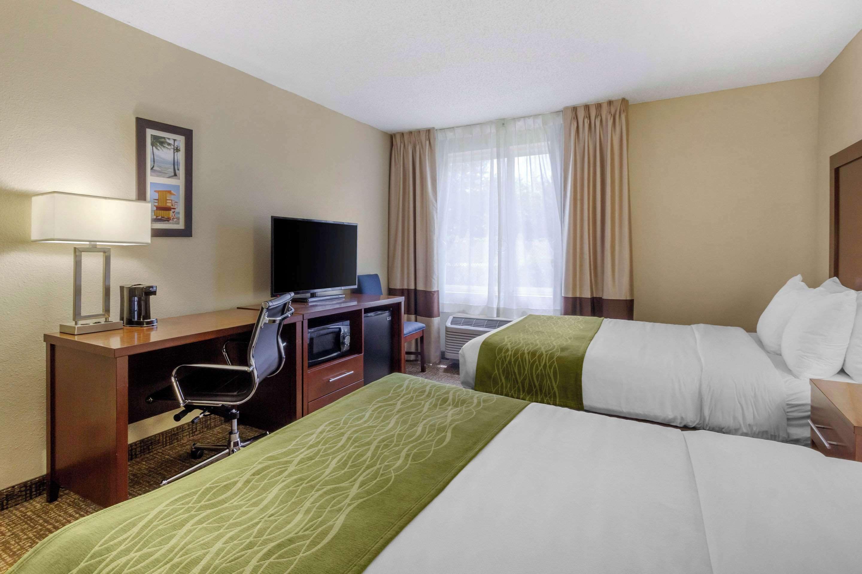A hotel room with two beds, a desk with a chair, a television, and a window with curtains.