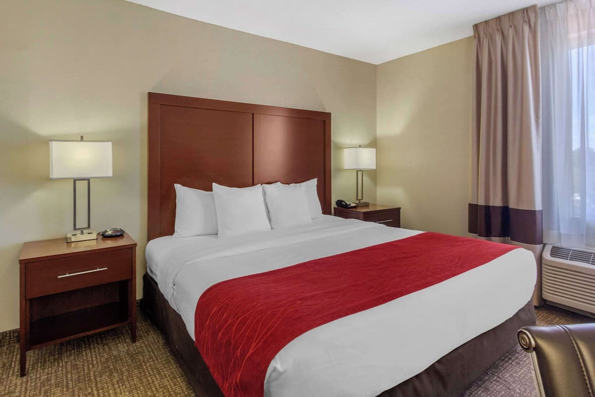 Habitación de hotel con una cama grande, dos mesitas de noche, una manta roja y una ventana con cortinas.