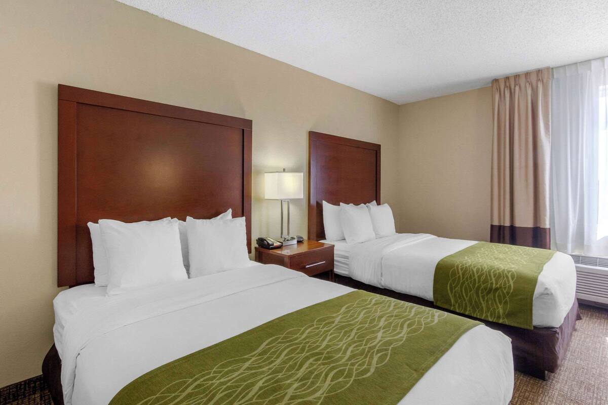 Habitación de hotel con dos camas, una mesita de noche, una lámpara y un ventanal con cortinas.