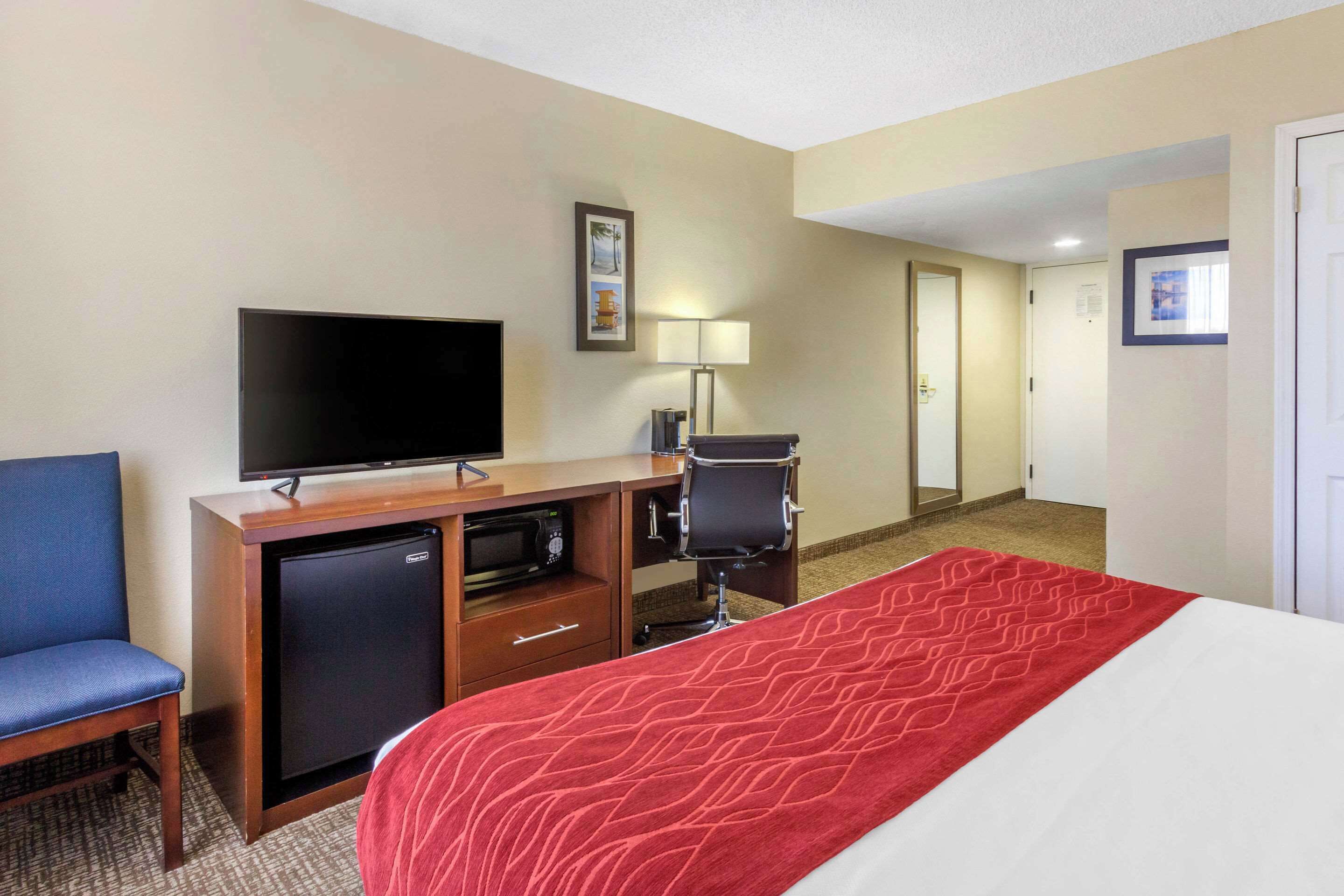 Habitación de hotel con cama, televisión, escritorio con computadora, silla y un refrigerador pequeño.