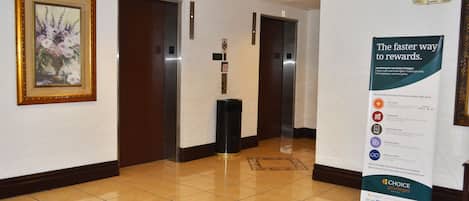 A hotel corridor with two elevators, a trash bin, and a promotional sign for Choice Privileges.
