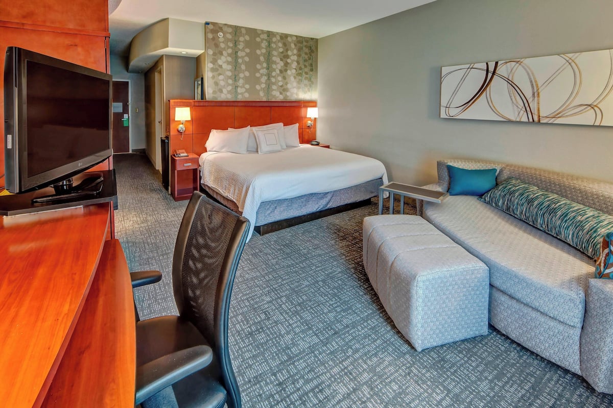Une chambre d’hôtel avec un lit, un canapé, un bureau avec une télévision et une chaise.