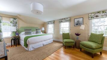 A bedroom with a large bed, two chairs, a lamp, and a window with curtains.