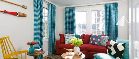 A living room with a red sofa, teal armchair, and a wooden coffee table with a vase of flowers.